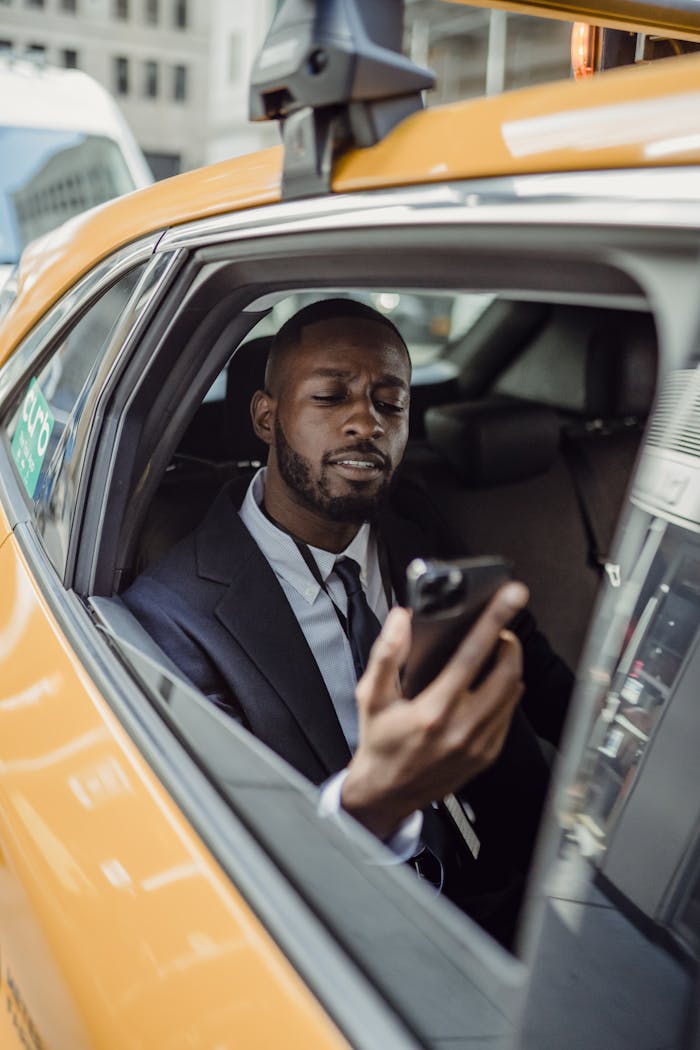 Young man in suit using phone inside a taxi in an urban setting. Daylight.